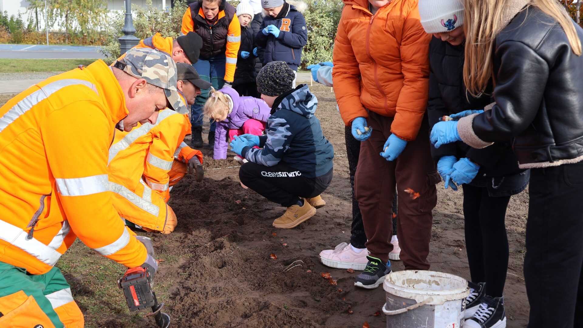Dzieci z pomocą dorosłych sadzące kwiaty na skwerze przy bibliotece w Pleszewie.