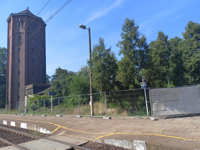 zdjęcie przedstawia wieżę ciśnień w Kowalewie oraz teren zielony, który będzie przeznaczony na parking w pobliżu stacji kolejowej