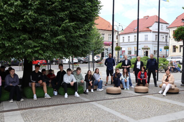 Grupa wykonująca pufki na pleszewskim rynku na tle swojego dzieła.